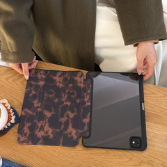 A 2 in 1 magnetic detachable ipad cover opened flat on a wooden table, displaying the dark tortoiseshell print inner lining separated from the clear tinted protective back shell.