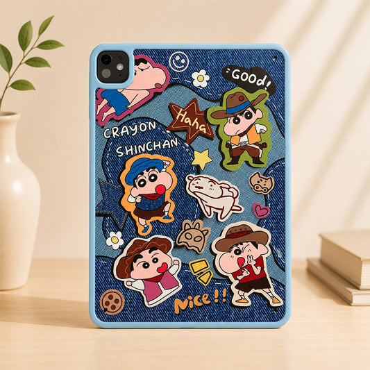 An upright studio product shot of an aesthetic Crayon Shin-chan denim print iPad case standing on a light wooden desk, with a minimal white ceramic vase on the left and stacked books under warm ambient light.