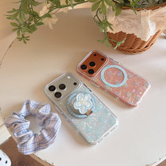 Flat lay of clear floral shell iPhone cases with a blue checkered scrunchie next to a woven flower basket.