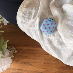 A pastel blue retro polka dot AirPods case resting elegantly on a textured white lace fabric over wood.