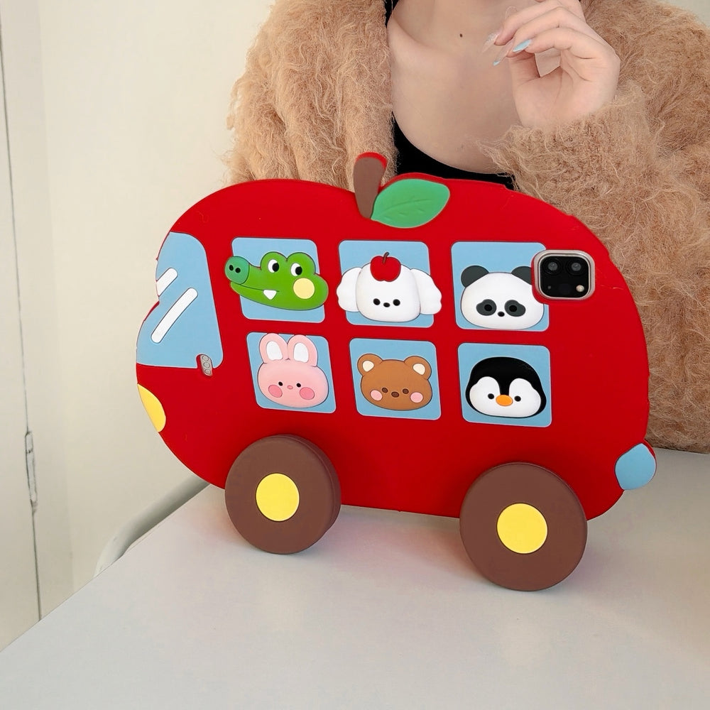 Front view of the red apple bus tablet cover standing upright on a white desk using its built-in wheel kickstands, with a person in a fuzzy sweater behind it.