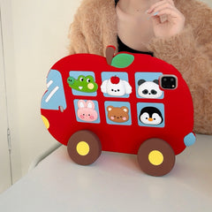 Front view of the red apple bus tablet cover standing upright on a white desk using its built-in wheel kickstands, with a person in a fuzzy sweater behind it.