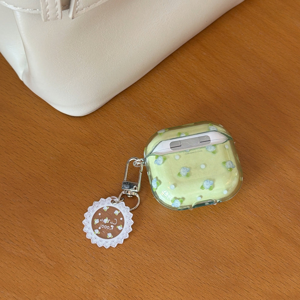 The back view of a green floral AirPods case lying on a wooden surface next to a white leather bag.