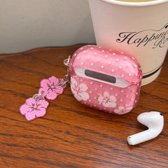 The back view of a pink floral AirPods case showing the hinge, placed next to a coffee cup and one earbud.
