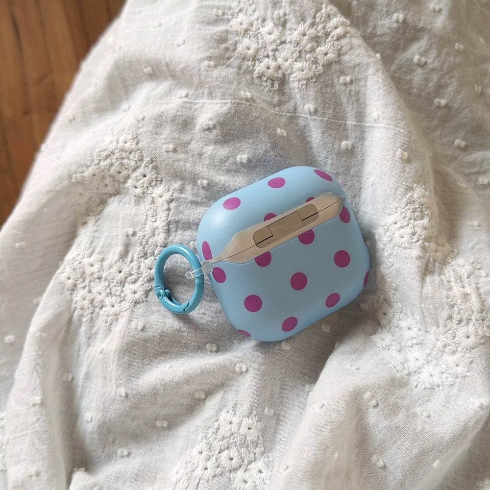 The back view of a blue polka dot AirPods case showing its clear hinge mechanism on white lace.