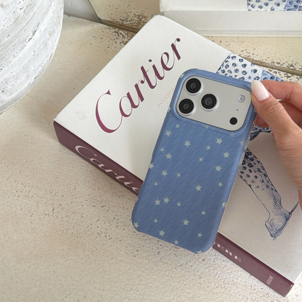 A hand holding a blue star pattern phone case showing the camera module on top of a book.