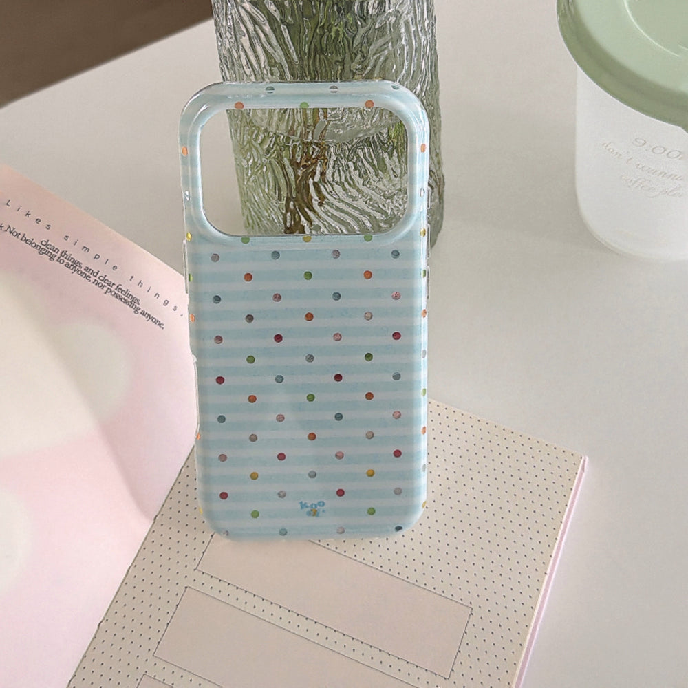 An empty blue stripe phone case shell propped open on a notebook next to a glass vase.