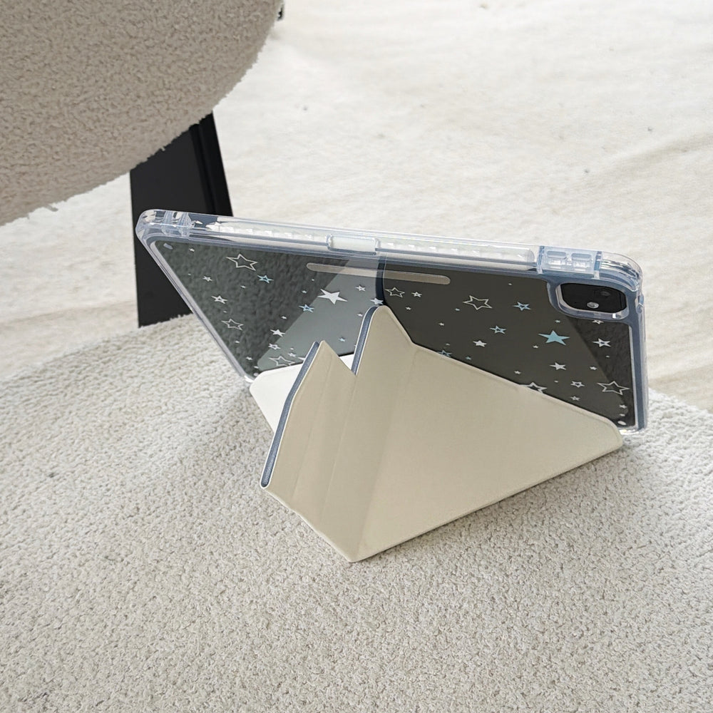 Rear view of a clear back shockproof iPad case with white star prints supported horizontally by a cream origami stand on a fuzzy white fabric.