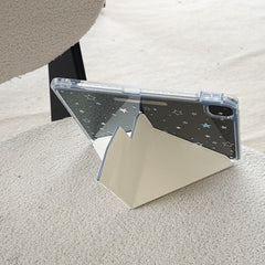 Rear view of a clear back shockproof iPad case with white star prints supported horizontally by a cream origami stand on a fuzzy white fabric.
