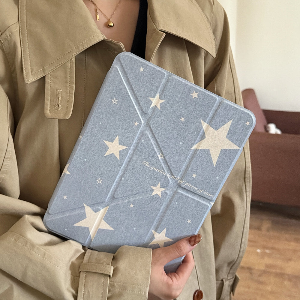 A person holding a coquette aesthetic starry sky iPad folio cover close to their chest against a khaki trench coat background.