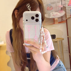 A girl taking a mirror selfie holding a coquette-style glitter phone case with pink magic keys and a beaded charm strap.