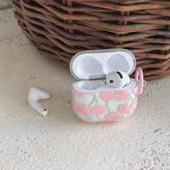An open coquette cherry AirPods case displaying a white earbud next to a rustic wicker basket.