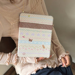 A lifestyle shot of a woman in a ruffled beige coquette-style top holding a closed cute kawaii teddy bear iPad case, emphasizing the trendy aesthetic appeal of the product's design.