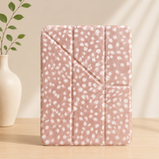 A closed cottagecore deer spot print origami iPad case standing vertically on a wooden table next to a white ceramic vase with green leaves.