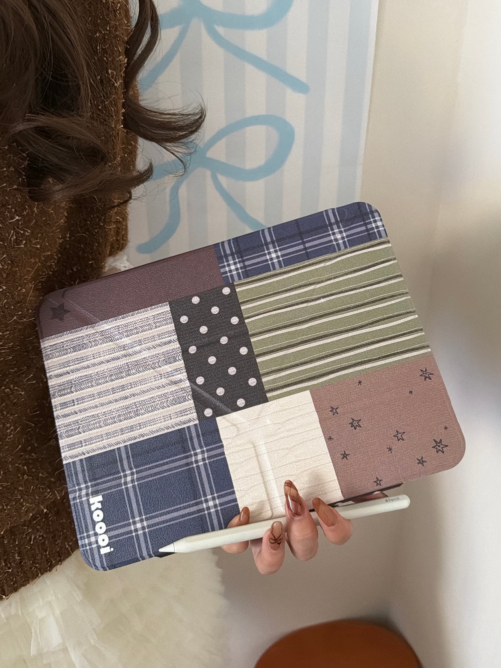 A close-up view of a person holding the closed cottagecore patchwork plaid iPad case horizontally, pairing it with a white stylus pencil at the bottom.