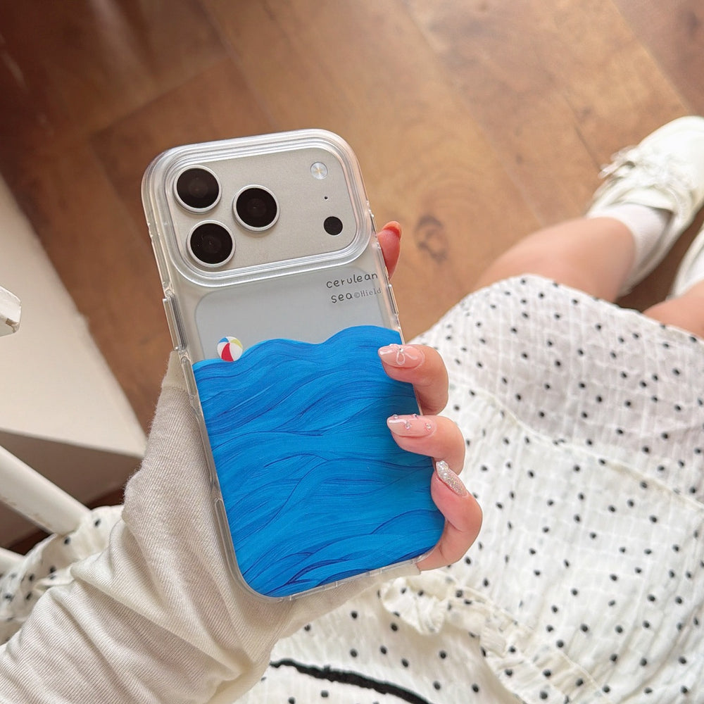 Top view of a woman in a polka dot dress holding a clear wave-printed phone case with a small beach ball graphic.