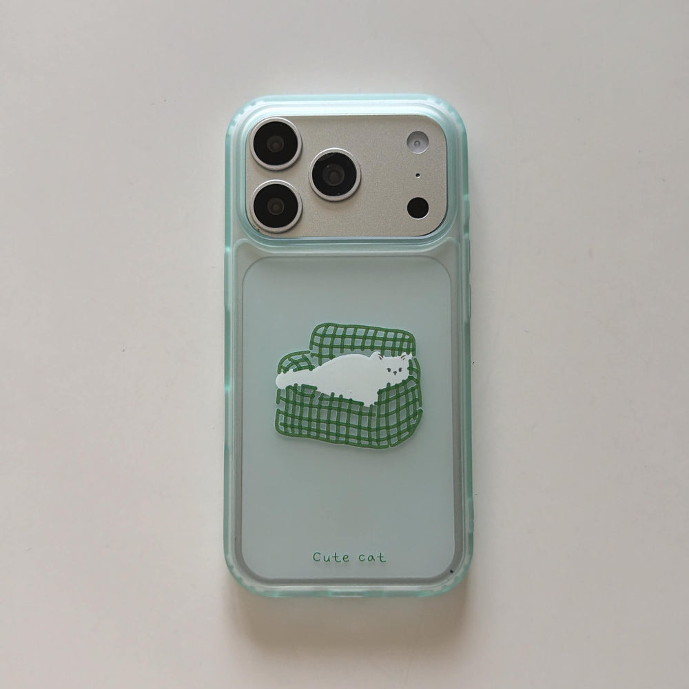 A flat lay view of a clear aesthetic iPhone case featuring a cute cartoon white cat on a green sofa on a white background.