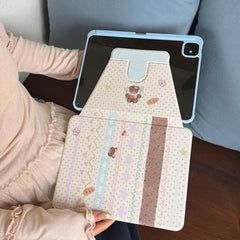 A person holding a fully unfolded aesthetic teddy bear iPad cover, displaying the seamless connection between the scrapbook pattern, the clear protective backing, and the smart magnetic flap.