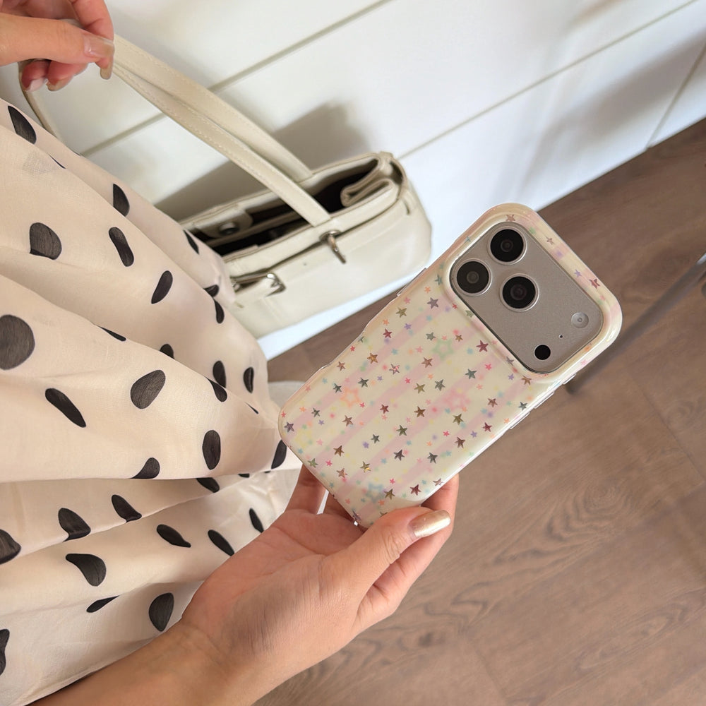 Hand holding a cute pastel star phone case at an angle next to a cream white leather handbag.