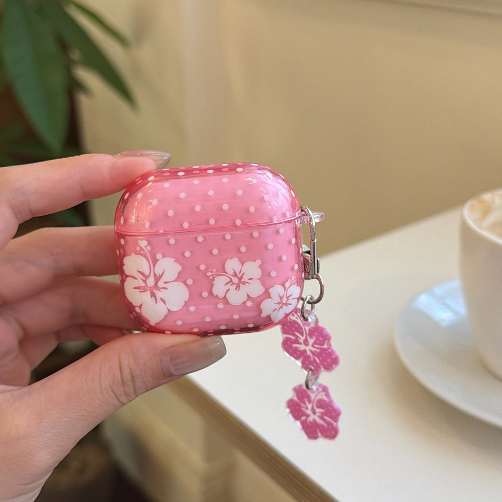 A hand holding a translucent pink hibiscus flower AirPods Pro case with a double flower charm keychain.