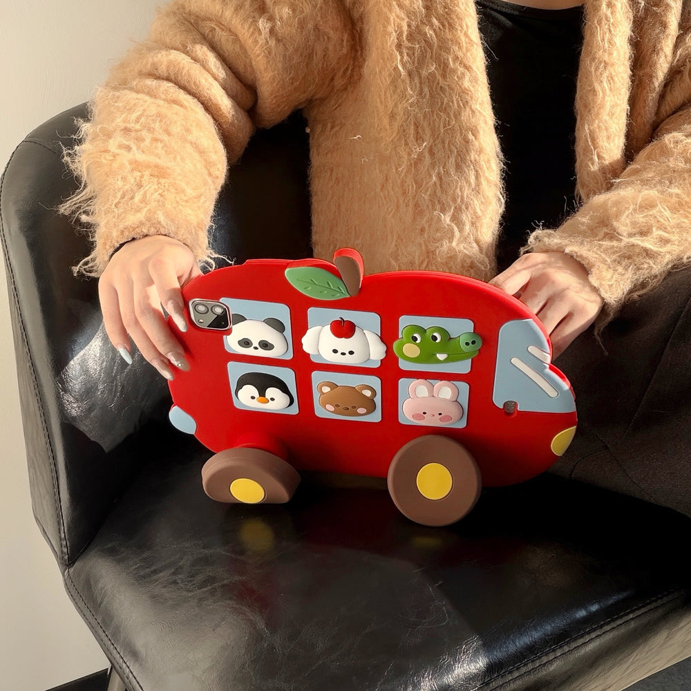 A person holding the cute red bus iPad case upright on a black leather armchair, displaying the full front design with its charming 3D animal window graphics.