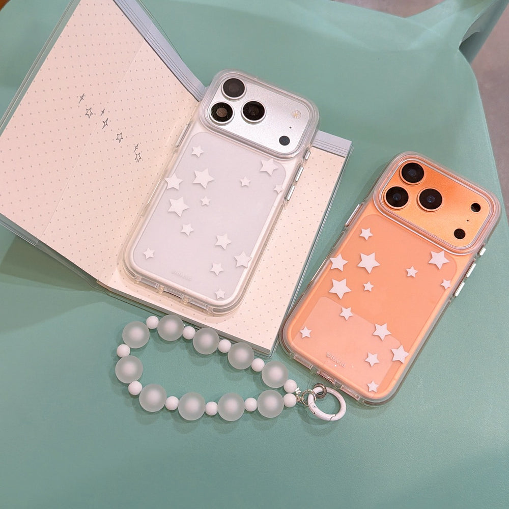 An orange and a silver clear phone cover with scattered white stars displayed next to an open notebook.