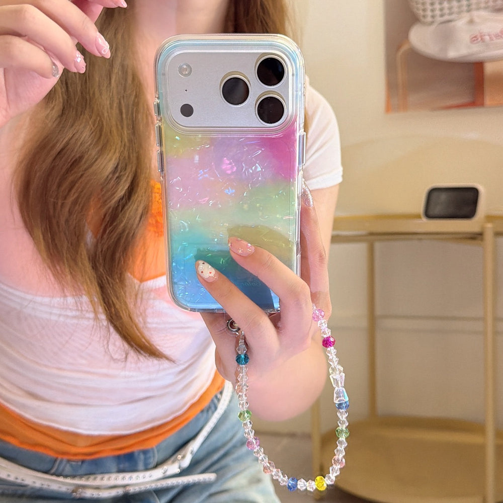 A woman holding a fairy-core rainbow gradient iPhone case with a silver lens frame, decorated with a clear and colorful crystal beaded wristlet.