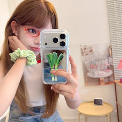 A girl holding a funny green leek vegetable mirror phone case during a casual lifestyle mirror selfie.