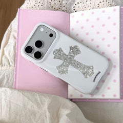 A gothic punk white phone case with a textured silver cross lying on a pink polka dot notebook.