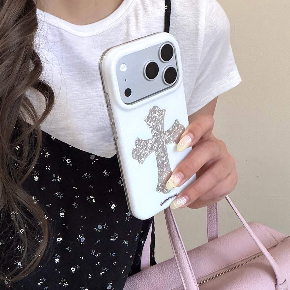 A person holding a white Chrome Hearts style cross iPhone case vertically next to a pink leather bag.
