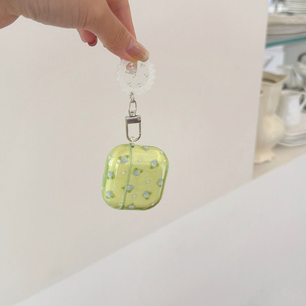 A hand dangling a green flower-patterned AirPods case by its clear round lace charm.