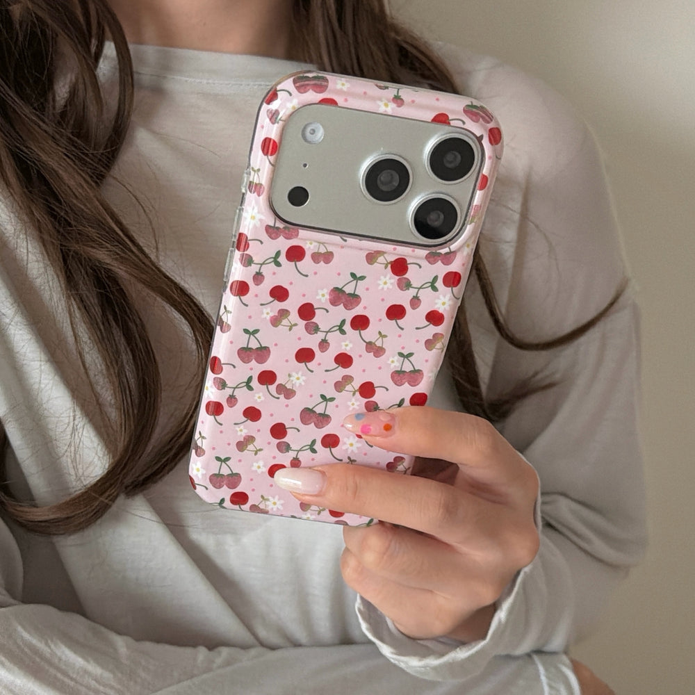A close-up view of a person holding a kawaii pink cherry iPhone cover showing an aesthetic pattern.