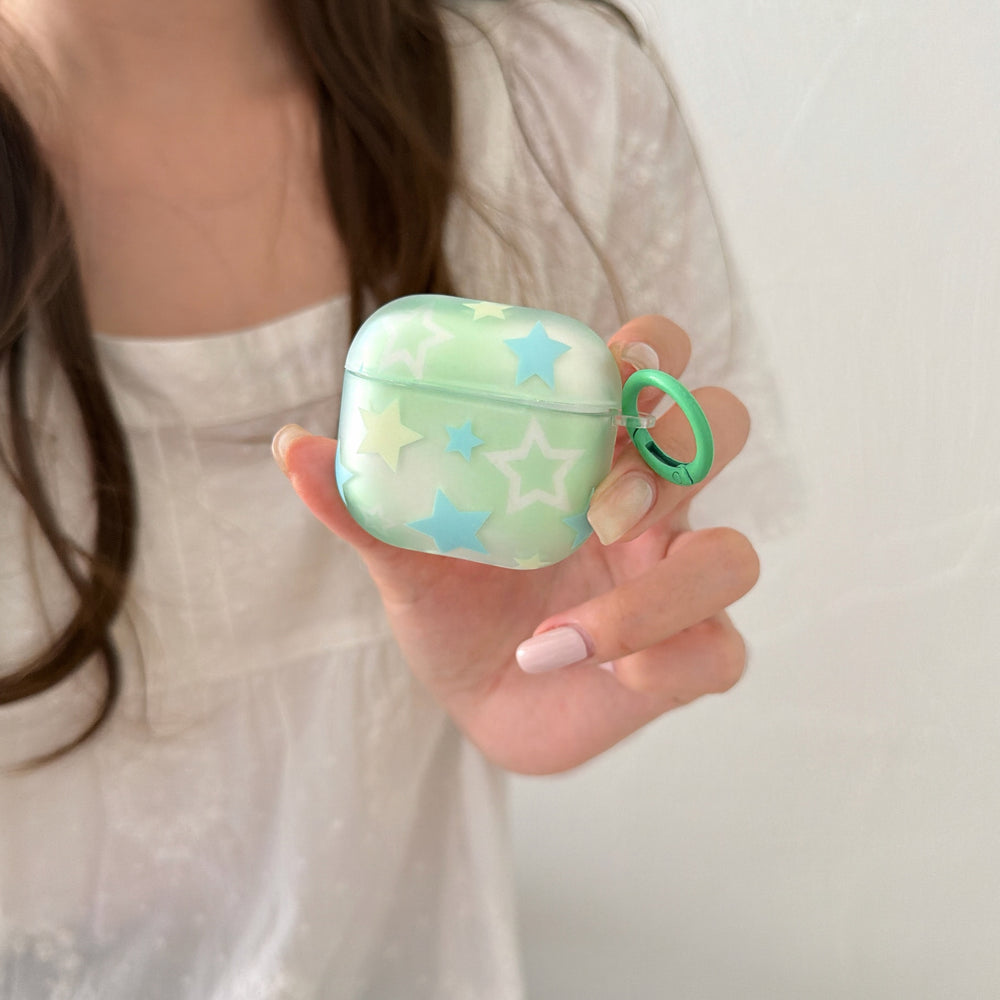 A close-up of a person holding a kawaii mint green star AirPods case against a white dress.