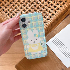 A hand holding a pastel blue plaid cartoon bunny iPhone case over a wooden surface.