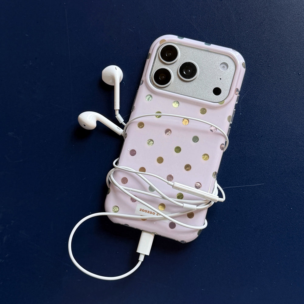 A holographic polka dot iPhone case wrapped in white headphone cords over a dark blue background.