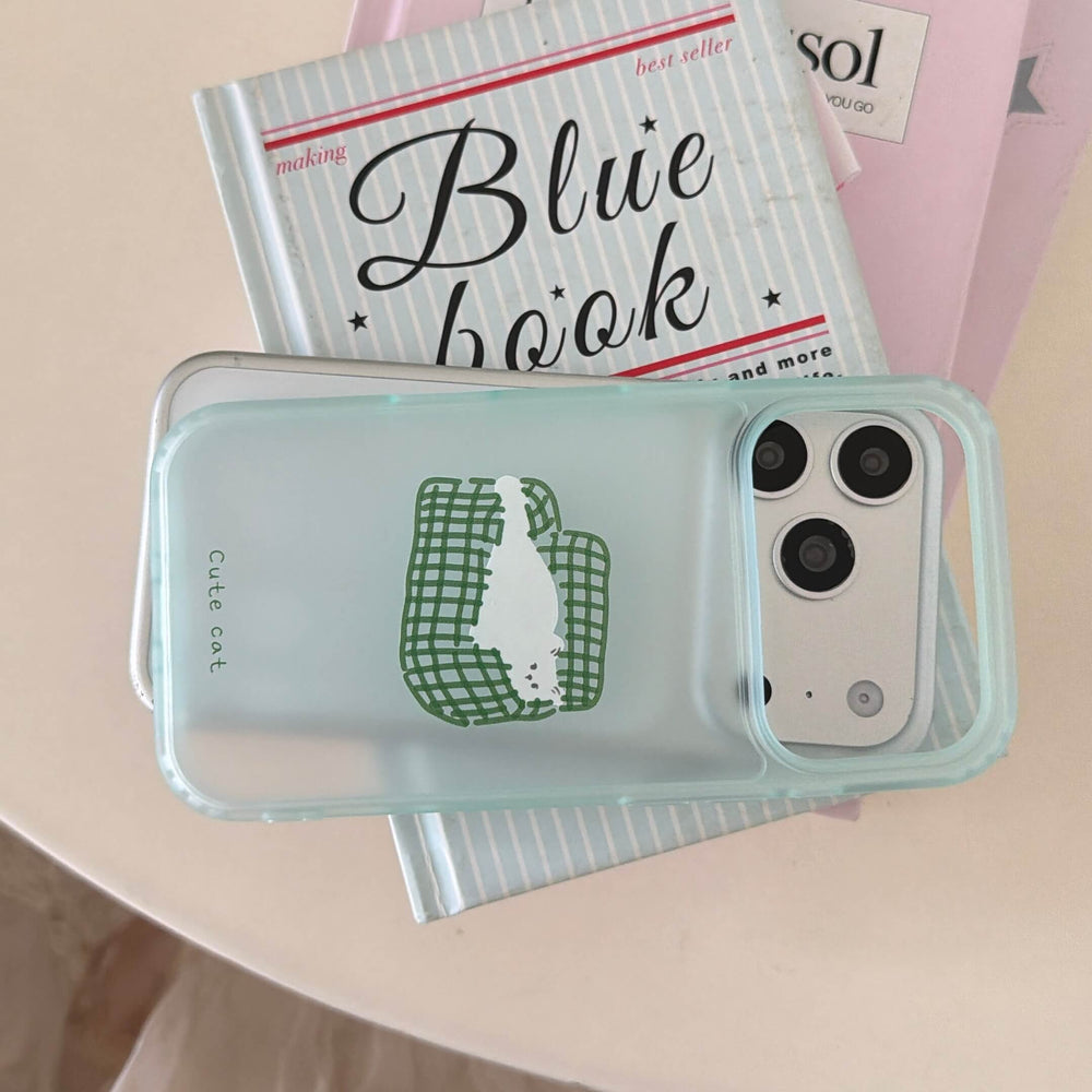 A horizontal view of a clear lazy cat iPhone case resting on a blue book.