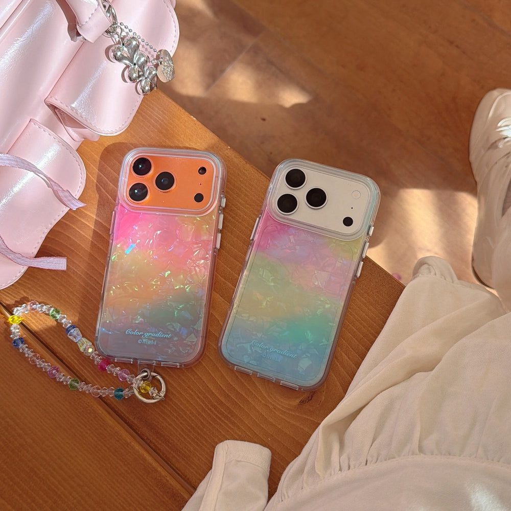 Two iridescent opal gradient iPhone cases with orange and white camera decks lying flat on a wooden bench next to a pink handbag.