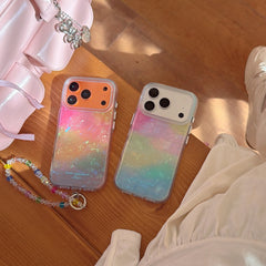 Two iridescent opal gradient iPhone cases with orange and white camera decks lying flat on a wooden bench next to a pink handbag.