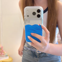 A girl holding a clear silver iPhone case decorated with hand-painted blue ocean waves and a small beach ball accent.