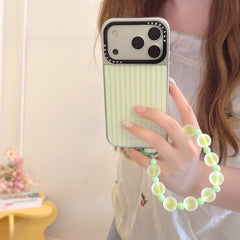 Close-up of a hand holding a kawaii green striped iPhone case featuring a silver lens frame and a matching wristlet.