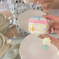 A hand holding a clear yellow gingham AirPods case with a pink drip design and a cute cat acrylic charm.