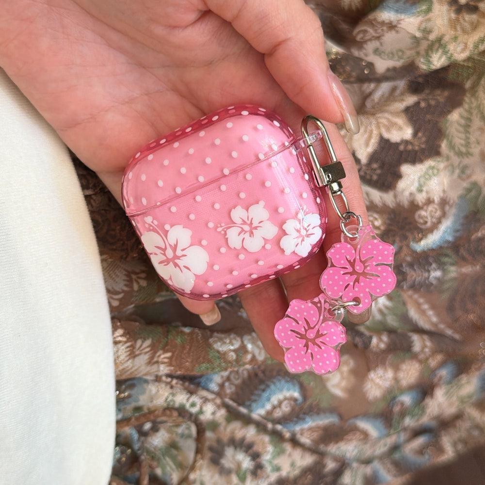 A close-up of a hand holding a kawaii pink Hawaiian flower AirPods case showing the side keychain attachment.