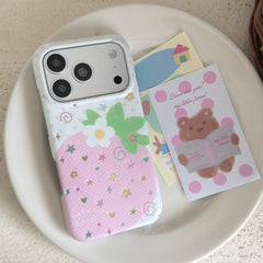 Top view of a kawaii pink strawberry iPhone case with a white camera frame resting on a ceramic plate next to a cartoon bear postcard.