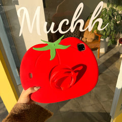 A kawaii red vegetable ipad shell held up in front of a glass boutique window with white cursive lettering, capturing the playful 3D tomato design under natural sunlight.