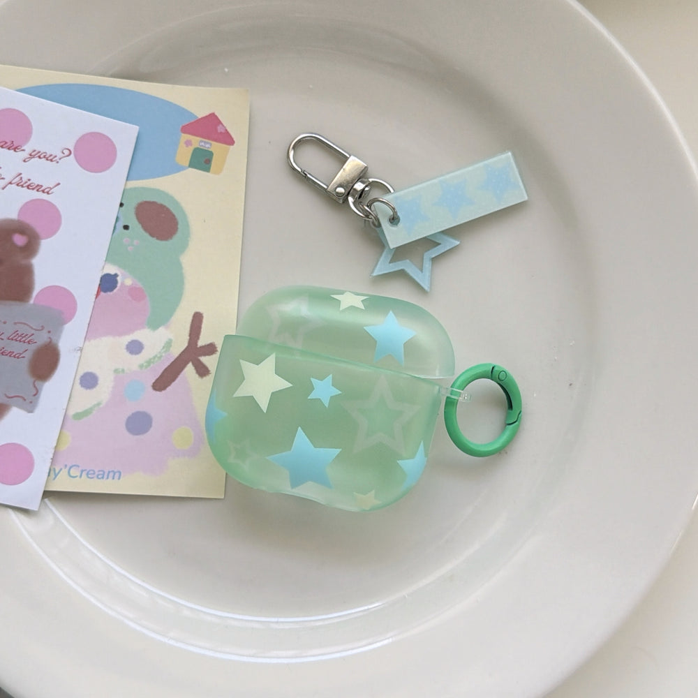 A translucent mint green AirPods case decorated with pastel stars and a matching star charm keychain on a white ceramic plate.