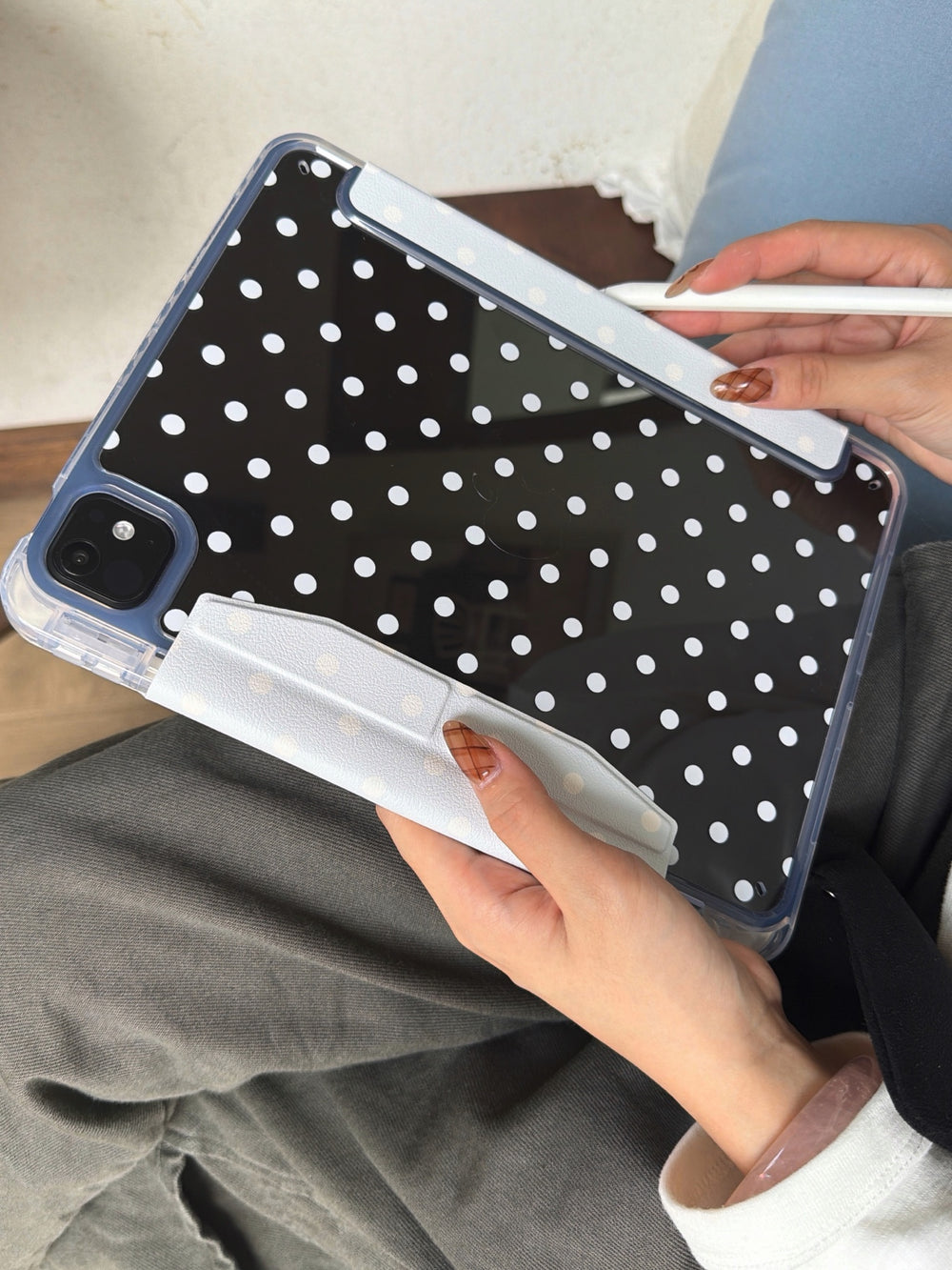 Hand holding the clear back of an iPad case with black and white polka dots, featuring light blue magnetic trims and a white stylus.