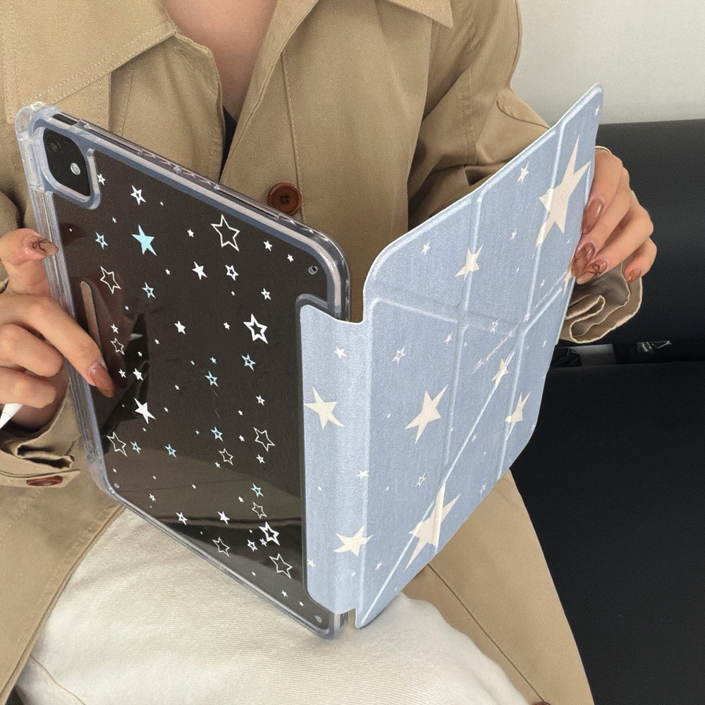A person wearing a trench coat holding a magnetic detachable iPad case showing the star-patterned clear back shell separated from the blue folio cover.