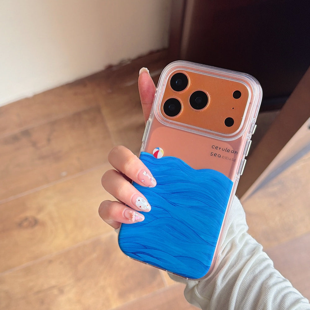 A hand holding a clear shockproof phone case showcasing a vibrant blue painted sea wave pattern on a bronze phone.