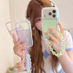 A girl holding a mint green phone case while displaying pink and purple clear bumper cases with beaded straps.