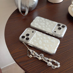 Two transparent phone covers with white flower sketches and a crystal beaded lanyard on a dark wooden table.